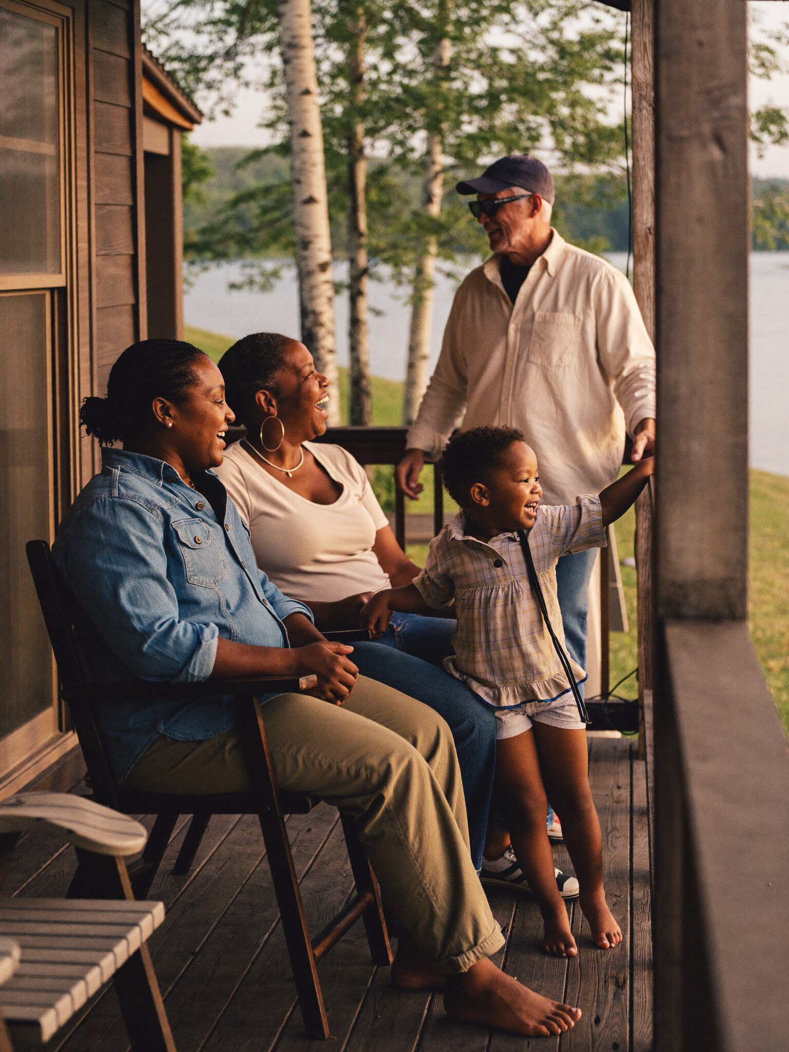 A multigenerational family laughing together on a lakeside porch at golden hour.