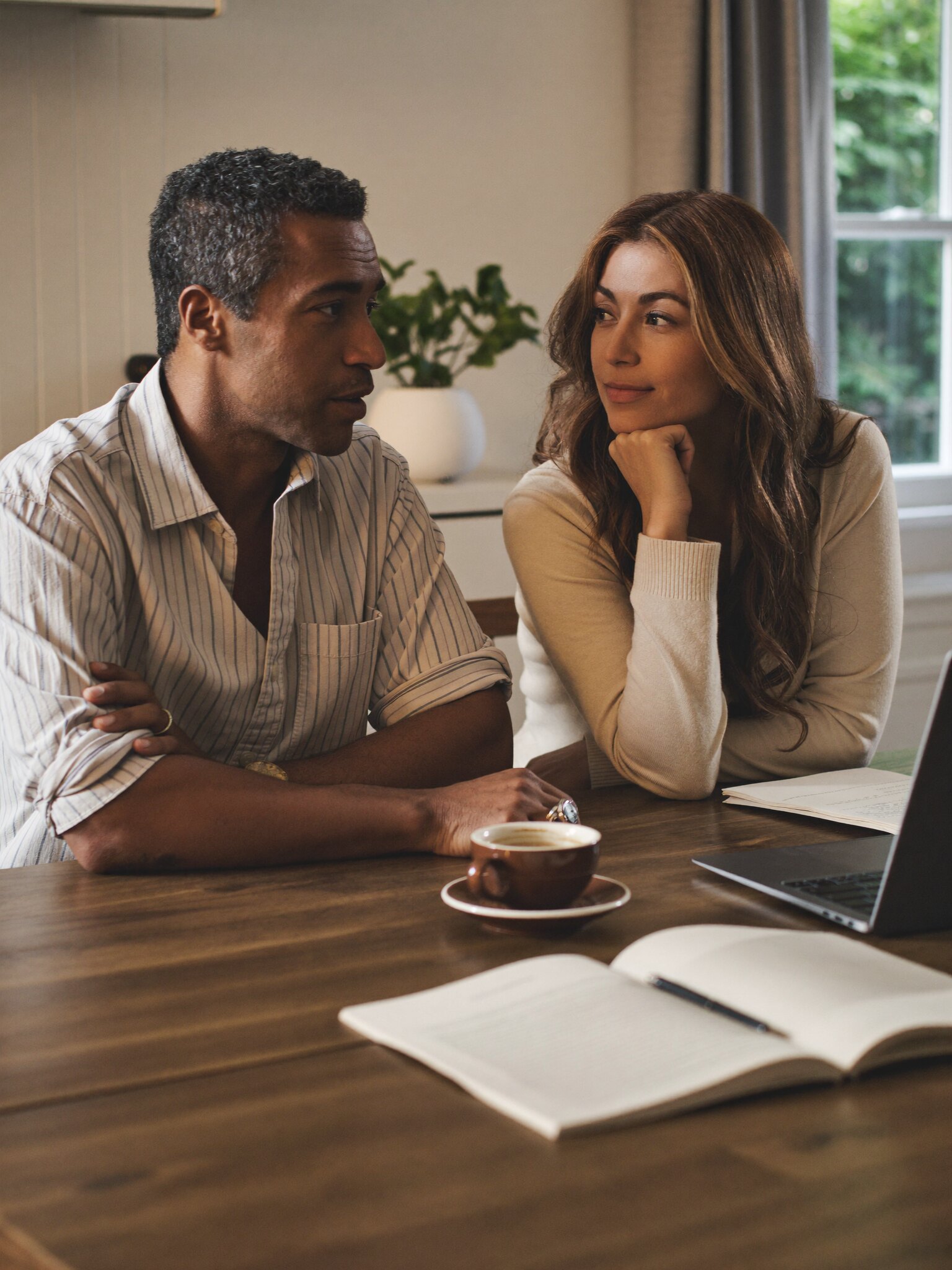 A couple reviewing paperwork together at their kitchen table in morning light.