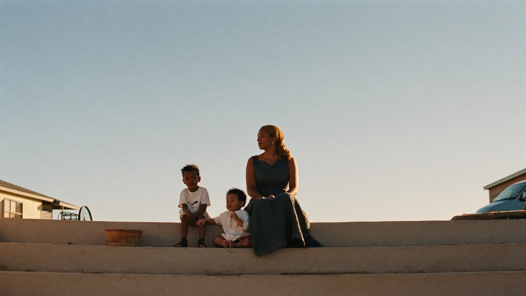A mother and her two young children sitting on porch steps against an open evening sky.