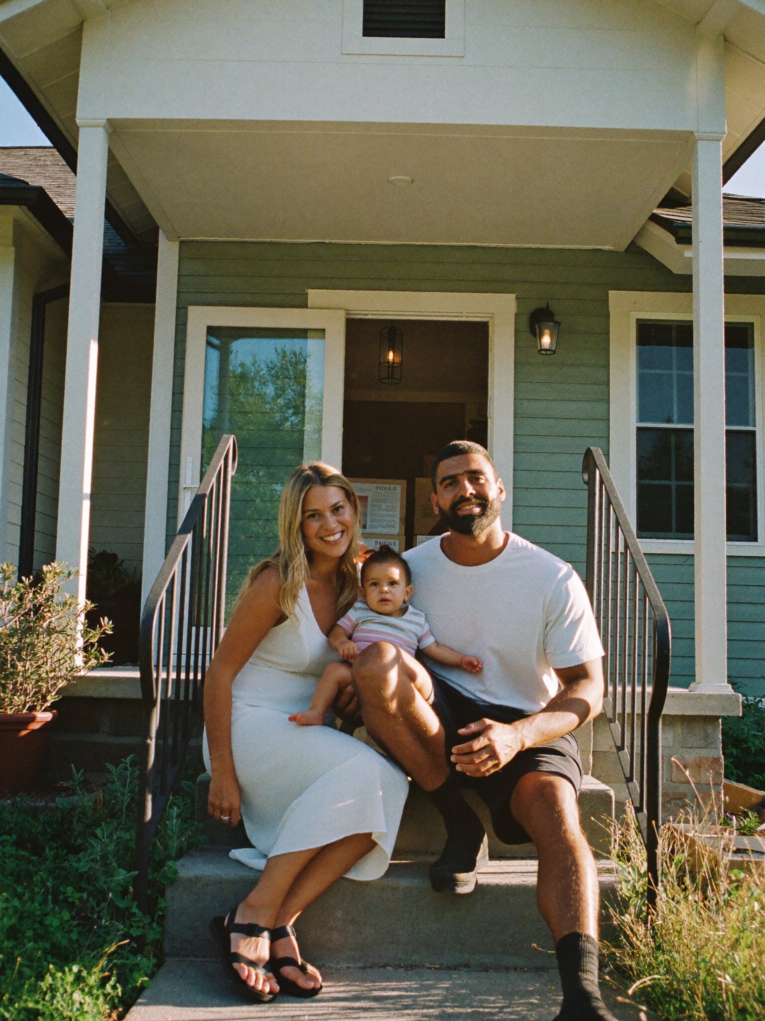 A young family sitting together on the front steps of their house.